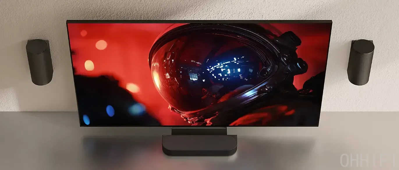 Sony Bravia Theatre Trio centre speaker mounted on the TV stand, with two cylindrical wall-mounted left/right speakers flanking the screen.