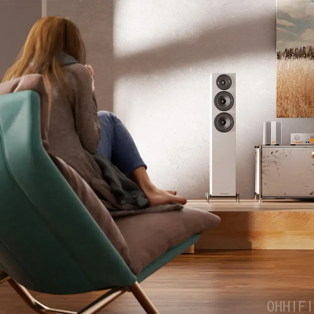 Person relaxing in a green armchair listening to a white Wharfedale floorstanding speaker beside a silver amplifier