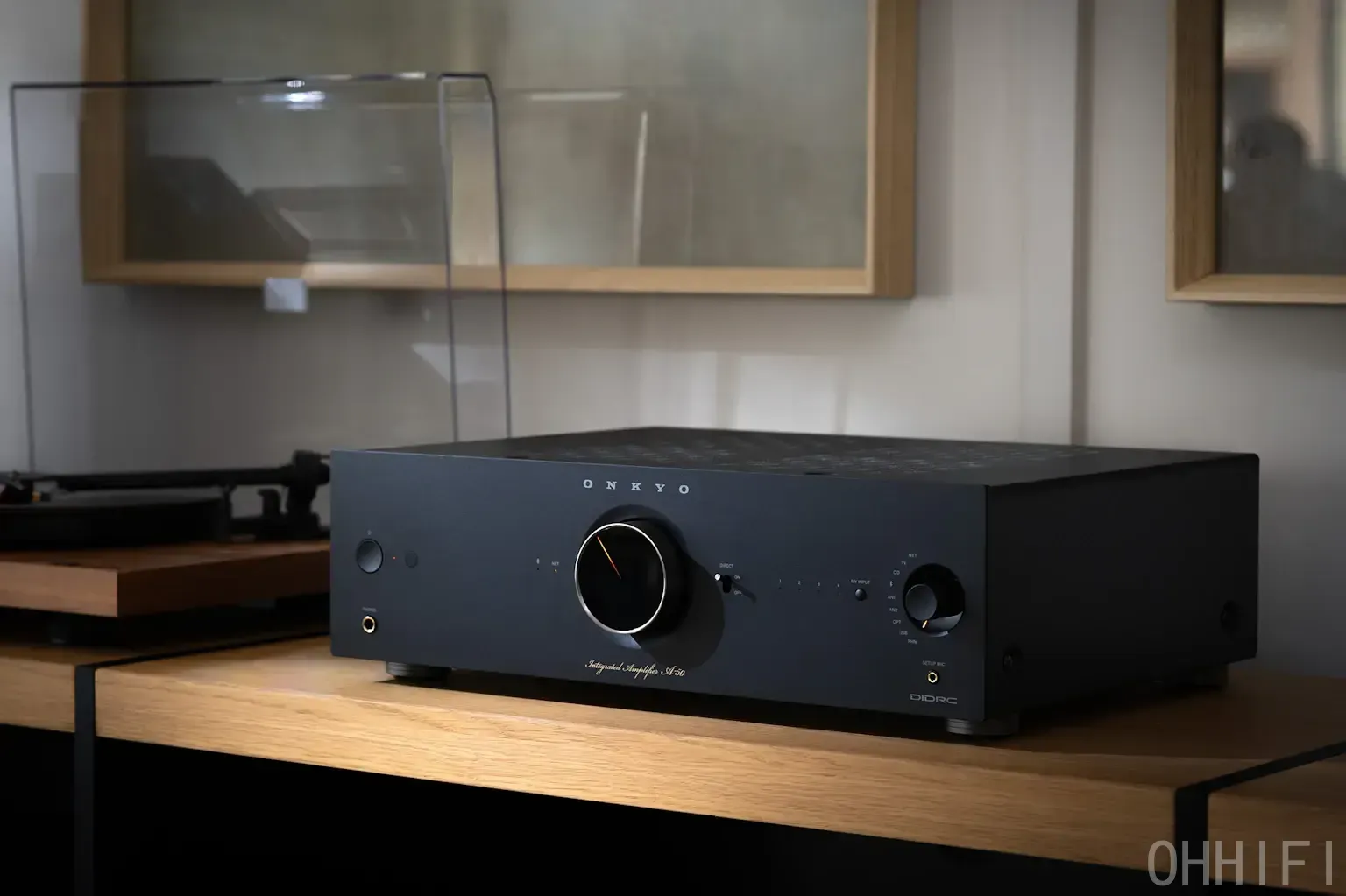Black Onkyo Icon A-50 integrated amplifier on an oak shelf next to a turntable, volume dial with orange pointer lit