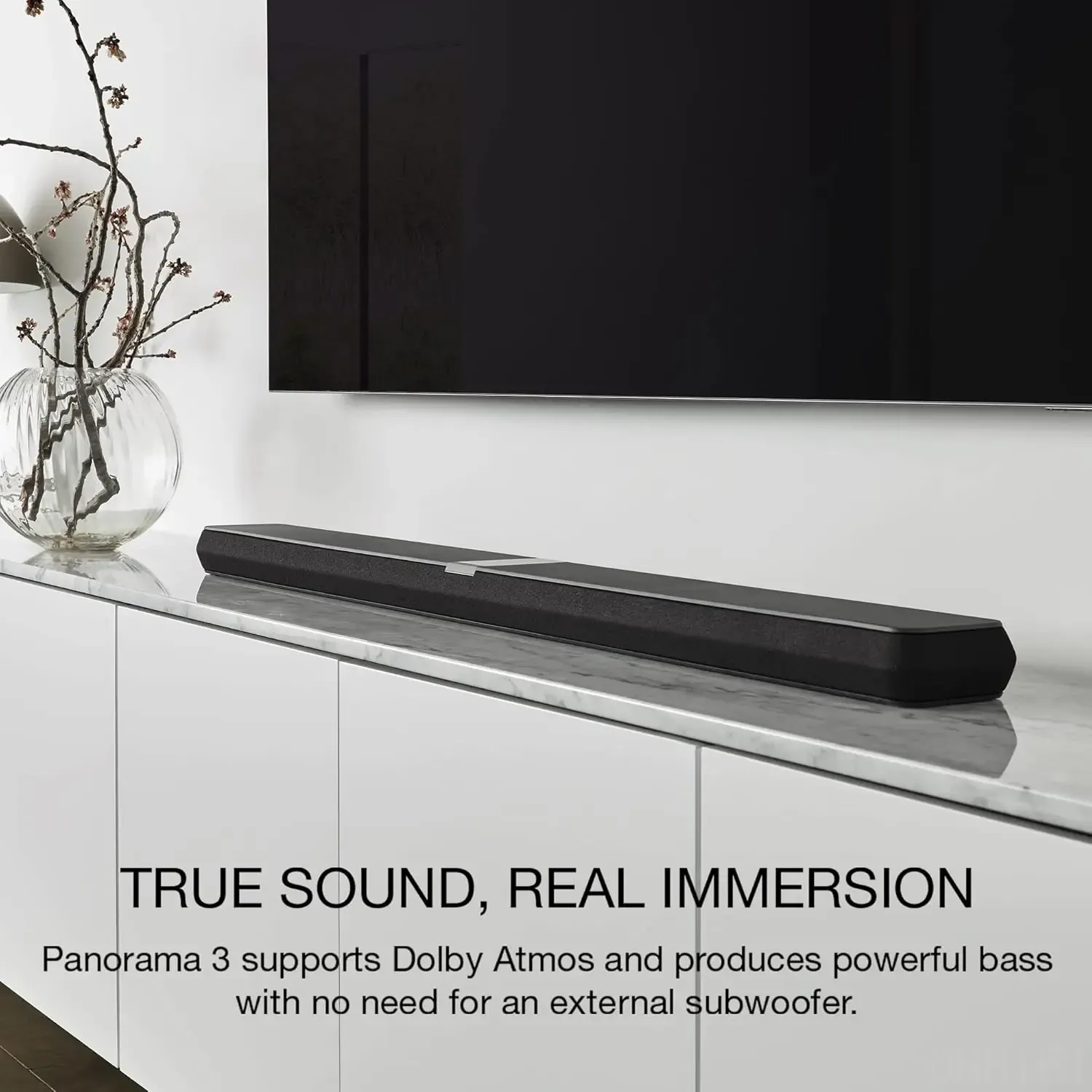 Bowers & Wilkins Panorama 3 black soundbar on a white marble console below a wall-mounted TV, beside a glass vase in a bright modern room.